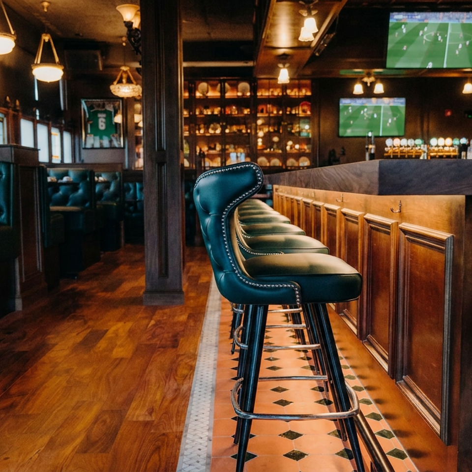 Elegant sports bar interior with teal leather bar stools, dark wood paneling, tiled floor, liquor shelves, and televisions showing soccer.