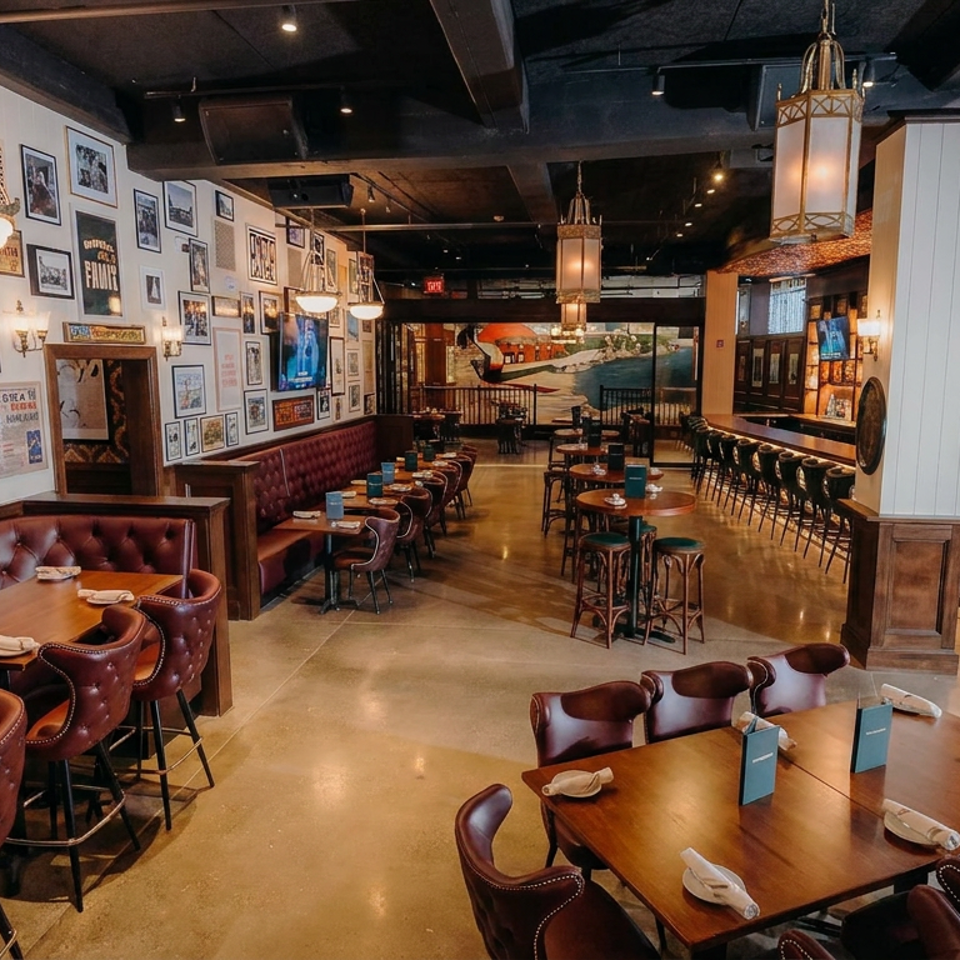 Spacious upscale restaurant interior with leather booths, wooden tables, framed artwork, pendant lighting, and a large bar.